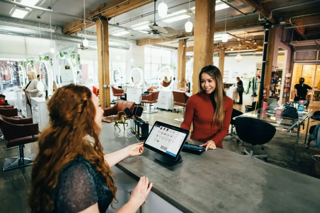 An image of 2 women in a corporate restaurant. one of them is touching a POS device on the table between them